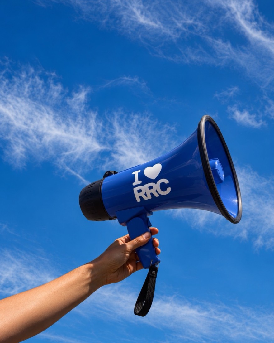 A hand holding a blue megaphone that says I love RRC against a bright sky