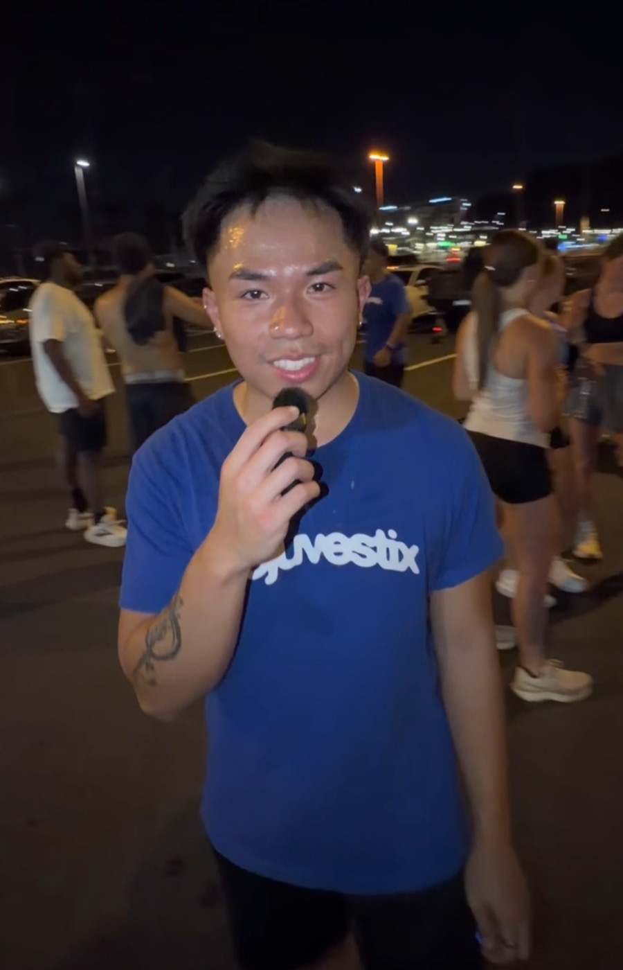 A runner in a blue Rejuvestix shirt answering into a mic in the parking lot after the run